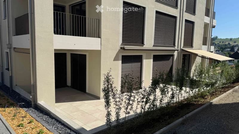 Modern multi-story residential building with balconies, large windows, and a covered entrance area.