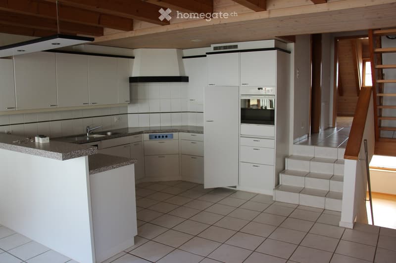 Modern kitchen with white cabinets, granite countertops, built-in oven, and a small staircase leading to another level.