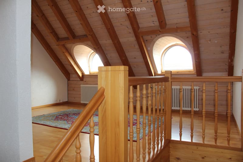 Spacious hallway with wooden floors, wooden staircase, arched windows, and radiators on the walls.