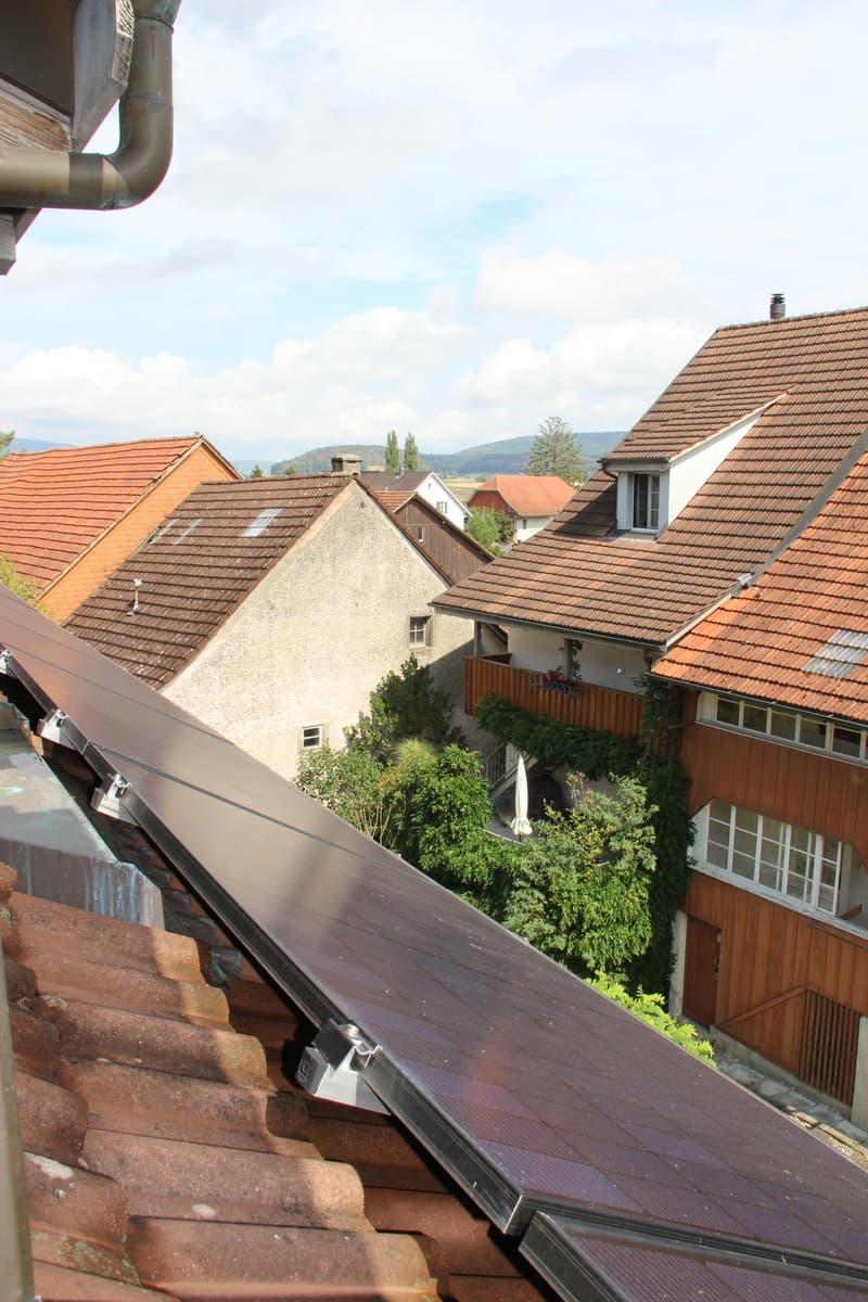 Residential neighborhood with multiple houses featuring red-tiled roofs, solar panels on one roof, and surrounding greenery.