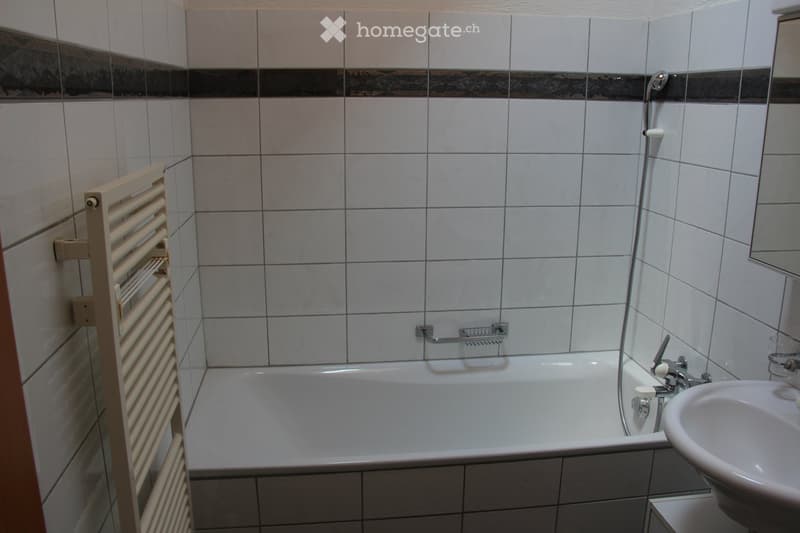 Bathroom with white tiled walls, a bathtub, a sink, a faucet, and a radiator on the left side.