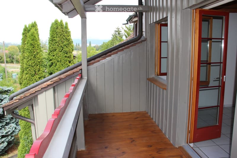 Balcony with wooden flooring, red railing, and a view of trees and the ocean.