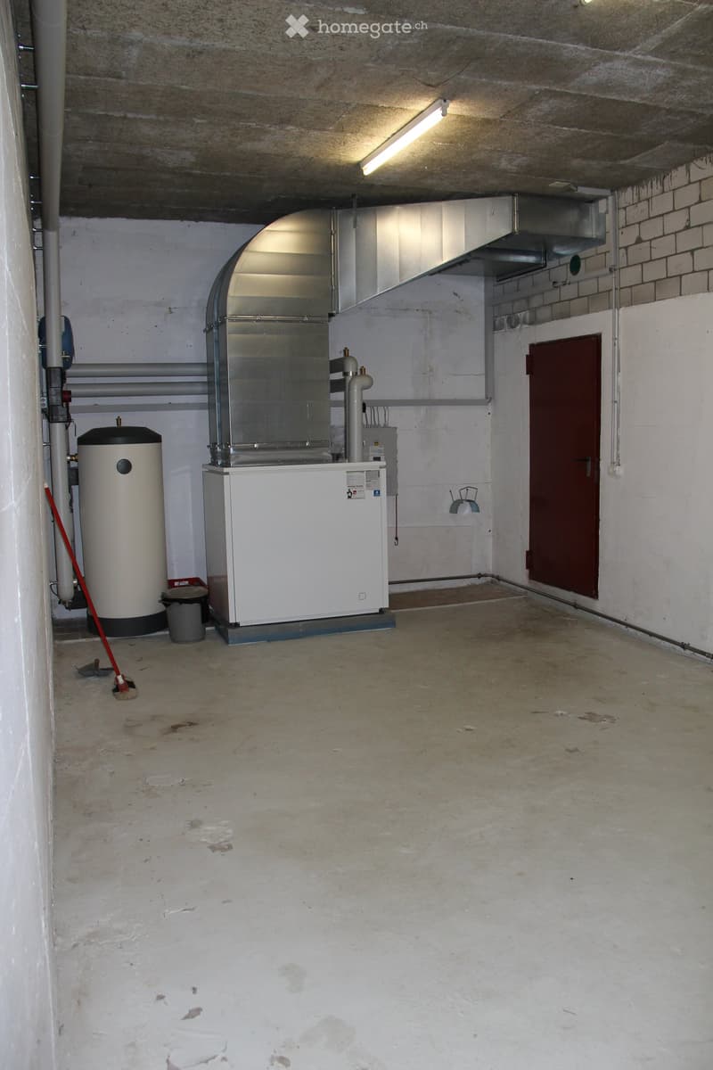 Empty basement room with concrete floor, white walls, and various utility equipment including a water heater, boiler, and ventilation system.
