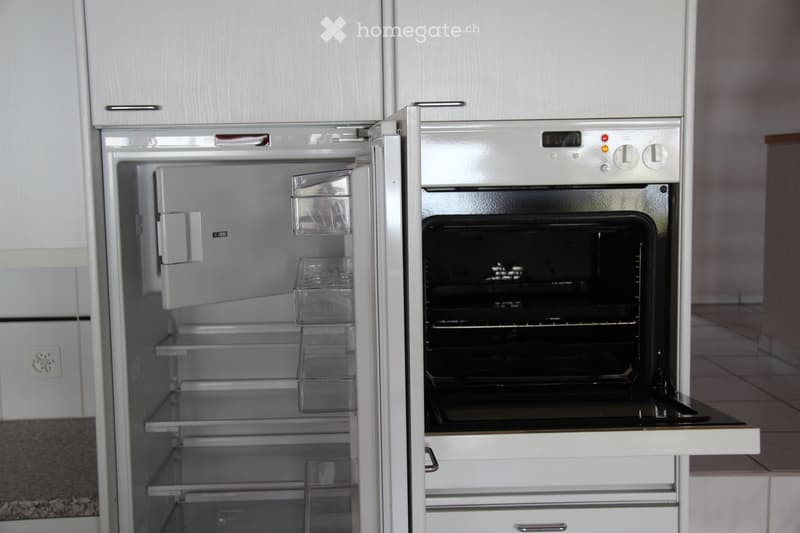 A modern kitchen with a stainless steel refrigerator and oven, both with their doors open, showing empty shelves and interior.