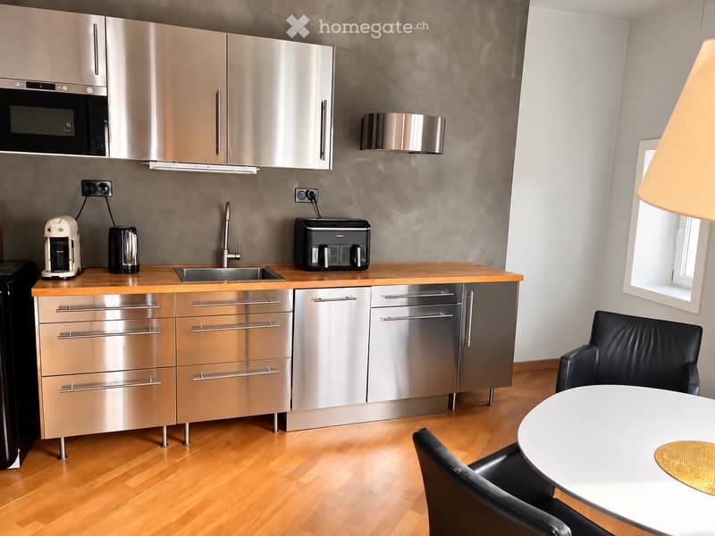 Modern kitchen with stainless steel appliances, wooden countertops, and a small dining area with a table and chairs.