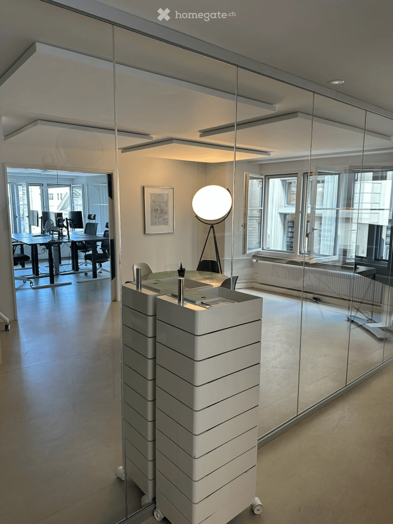 Modern office space with a sleek reception desk, chairs, a round table, and a large round lamp. Glass walls and large windows provide natural light.