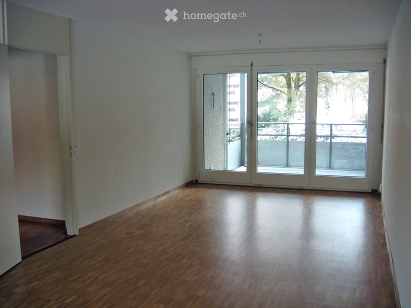 Empty room with wooden flooring and white walls, featuring large sliding glass doors leading to a balcony.