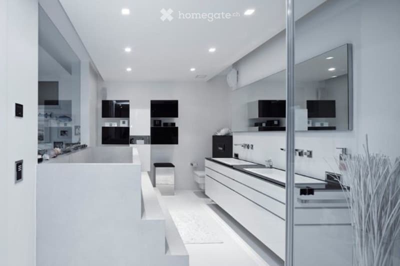 Modern, minimalist bathroom with white walls, a large bathtub, a sink, a toilet, and a mirrored cabinet. The space features sleek, contemporary design elements and ample natural light.