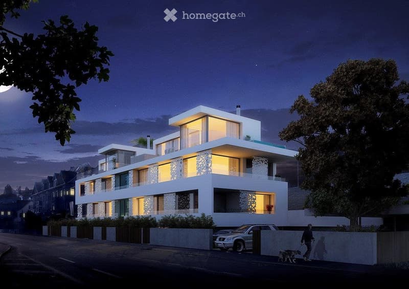 Modern, multi-story residential building with white exterior, large windows, and illuminated interiors. Features a raised ground floor and a parked car in front.