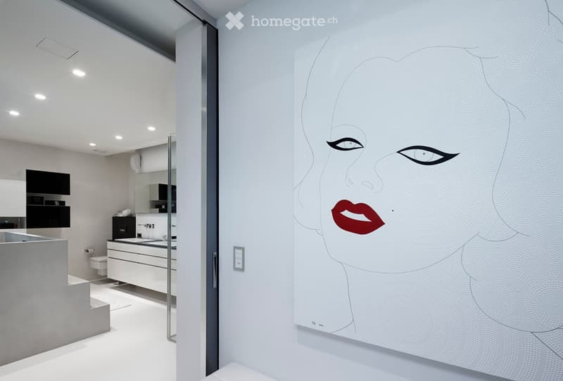 Modern bathroom with white walls, sleek sink, mirror, and a large decorative mural of a stylized face on one wall.