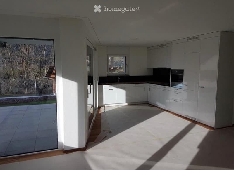 Empty kitchen with white cabinets, dark countertops, and large windows allowing natural light to fill the space.