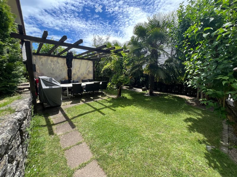 Well-maintained garden with a covered seating area, a grill, and lush greenery.
