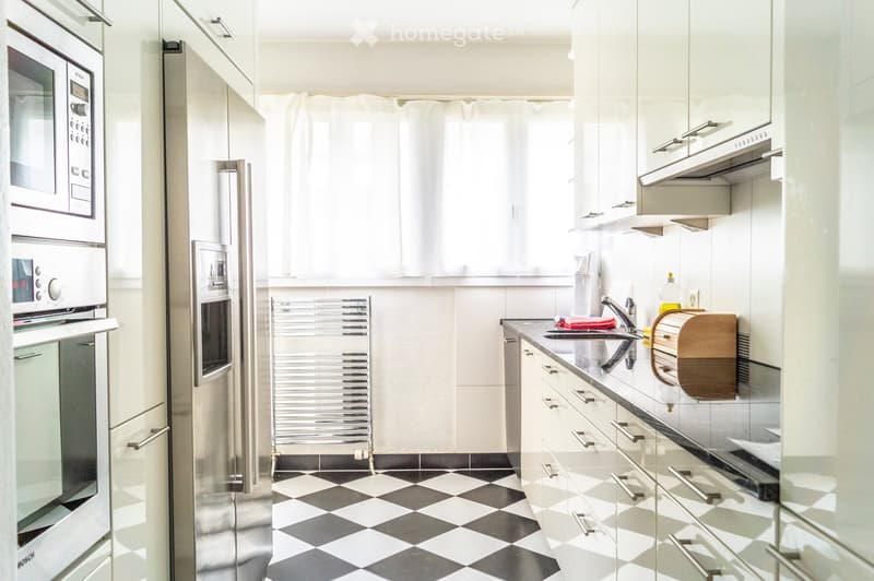 Modern kitchen with stainless steel appliances, white cabinets, and a black and white checkered floor. Features include a refrigerator, oven, microwave, sink, and a dish rack.