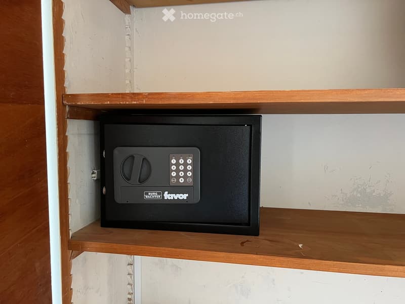Empty wooden shelf unit with a black electronic safe mounted on one of the shelves.