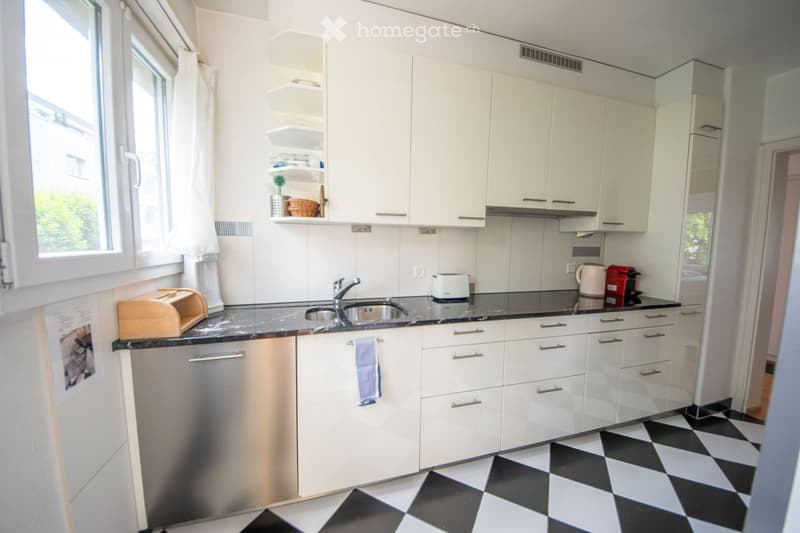 Modern kitchen with white cabinets, black countertops, and a stainless steel dishwasher. Features include a sink with a faucet, a toaster, a coffee maker, and a breadbox on the counter.