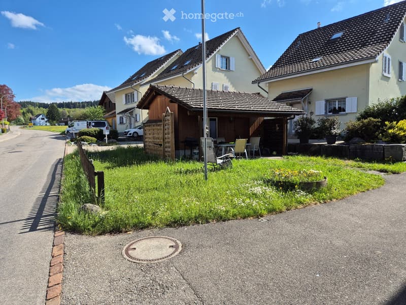 Residential street with houses, a wooden summerhouse, outdoor furniture, and a well-maintained garden area.
