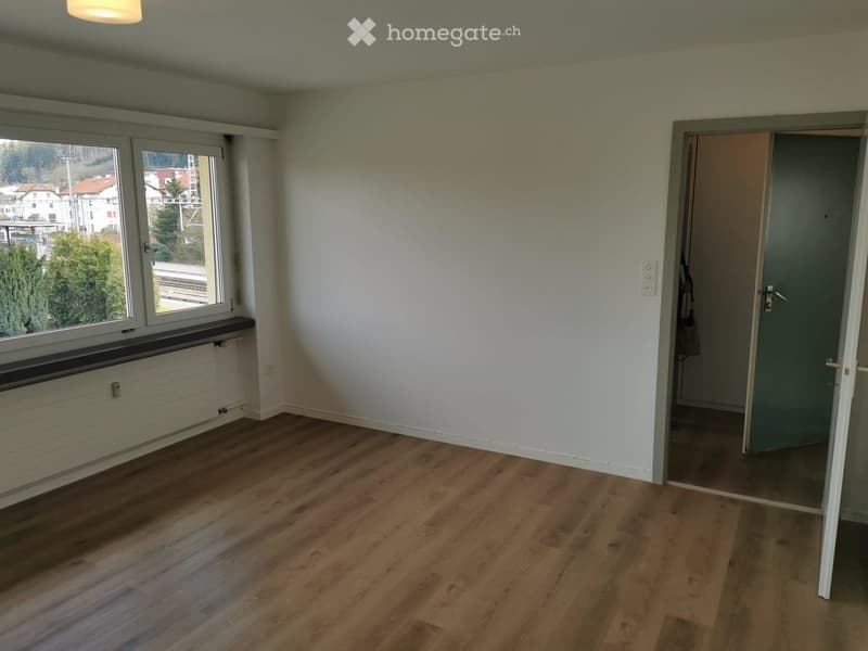 Empty room with large window, wooden floor, open door, white walls
