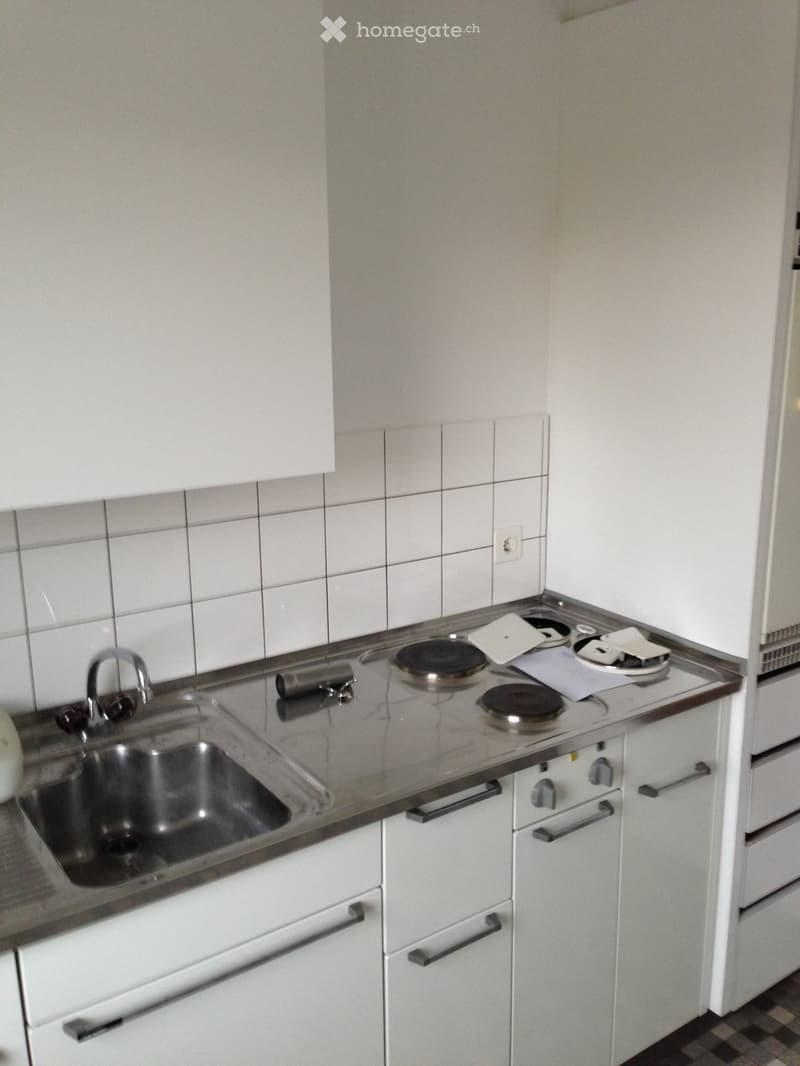 Small kitchen with stainless steel countertops and an integrated four-burner stove. It includes a stainless steel sink with a faucet and built-in cabinets with sliding doors.