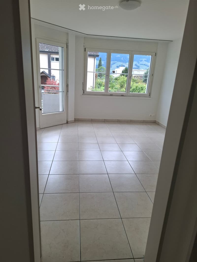Empty room with tiled floor, white walls, large windows, and a door leading outside.