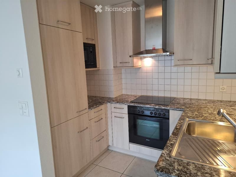 Modern kitchen with light wood cabinets, granite countertops, stainless steel sink, oven, microwave, and range hood.
