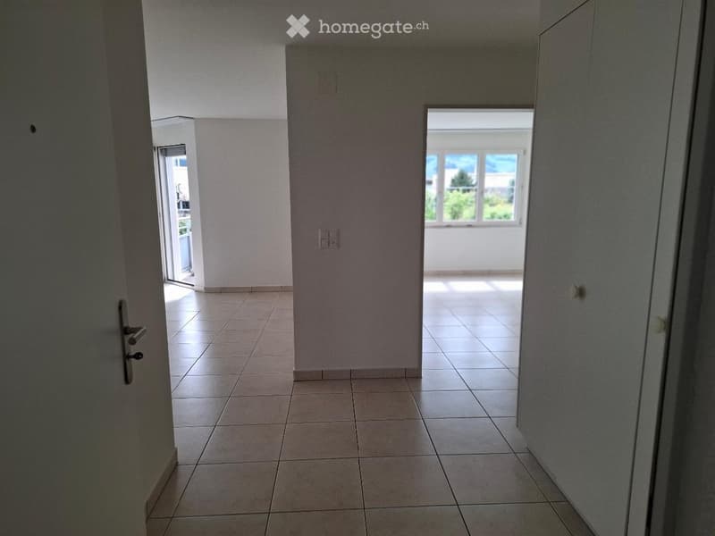 Empty hallway with tiled floor, white walls, and a large window at the end, allowing natural light to enter.