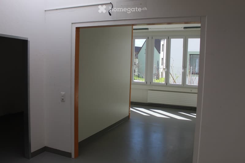 Empty room with white walls, dark floor, and large windows letting in natural light. No furniture or equipment present.