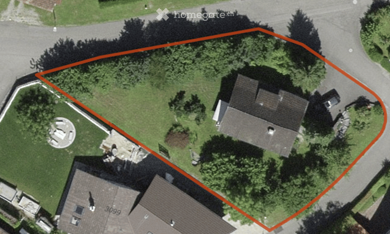 Aerial view of a residential property with a house, surrounding greenery, and a paved driveway.