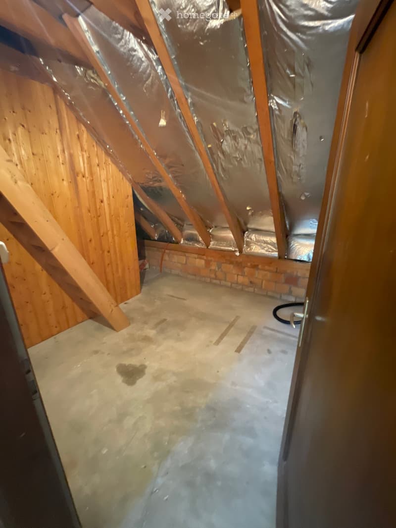 Empty attic space with exposed wooden beams, insulation, and a concrete floor. No furniture or equipment present.