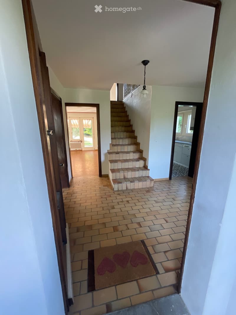 Hallway with tiled floor, wooden doors, staircase leading upstairs, and a small rug with heart designs.