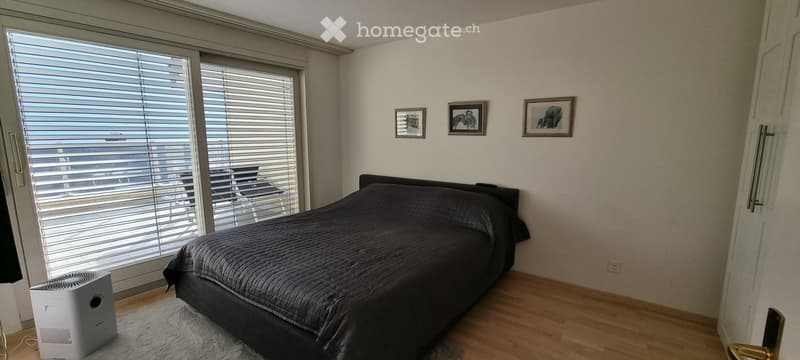 Modern bedroom with a large window, a neatly made bed, a fan, and three picture frames on the wall.