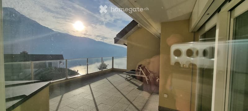 Balcony with a scenic mountain and lake view, featuring a glass railing and a wooden lounge chair.
