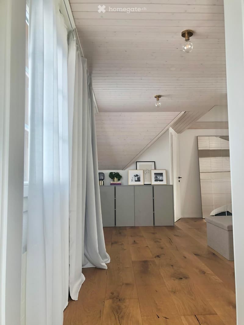 A modern, minimalist hallway with wooden flooring, white paneled ceiling, and a grey cabinet with picture frames and a small plant on top.