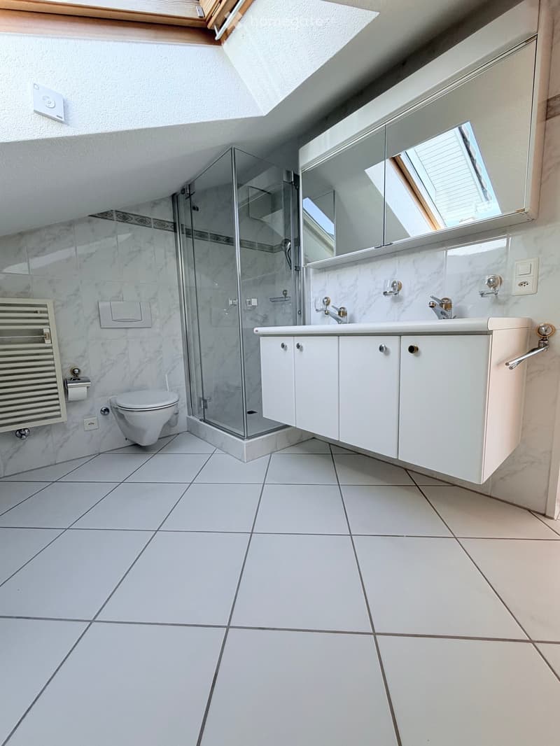 Modern bathroom with white tiles, a glass-enclosed shower, a toilet, a sink with a large mirror, and white cabinets.