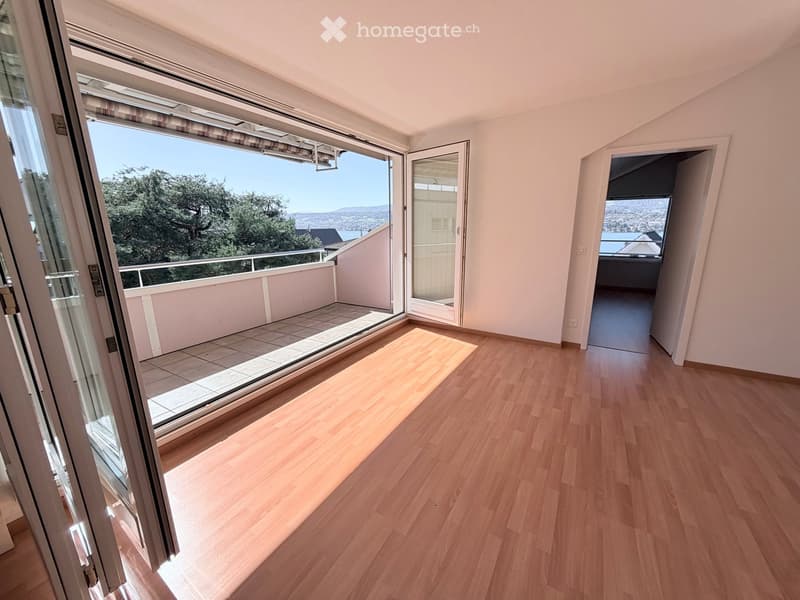 Empty room with wooden flooring, large sliding glass doors leading to a balcony with a scenic view of trees and distant landscape.