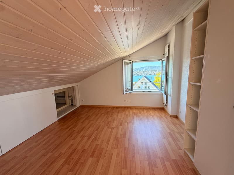 Empty room with wooden flooring, slanted wooden ceiling, built-in shelving unit, and large window offering a scenic view.
