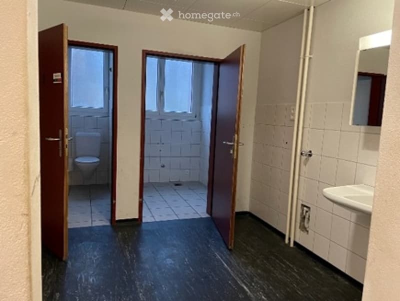 Empty room with dark flooring, white tiled walls, and two open doors leading to bathrooms.