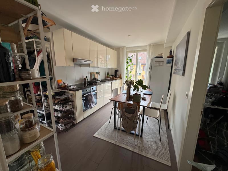 Modern kitchen with white cabinets, stainless steel appliances, a dining table with chairs, and a potted plant near the window.