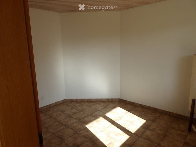 Empty room with tiled floor and white walls, featuring a wooden door frame and a small electrical outlet visible on the left wall.