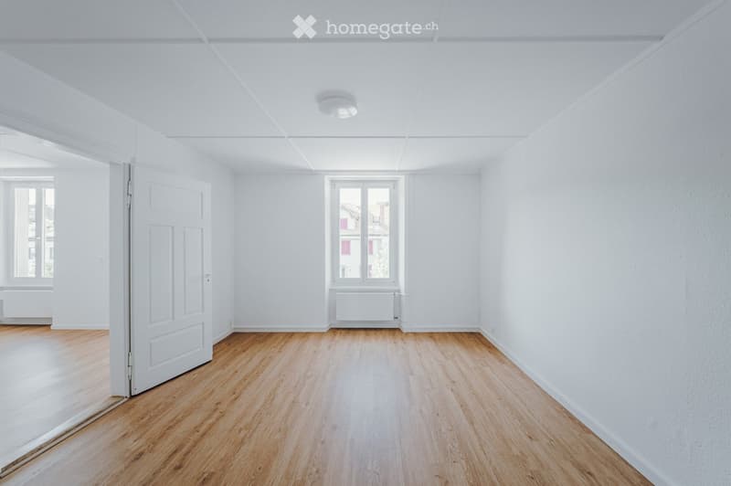 Empty room with white walls, wooden flooring, and large windows. No furniture or equipment present.