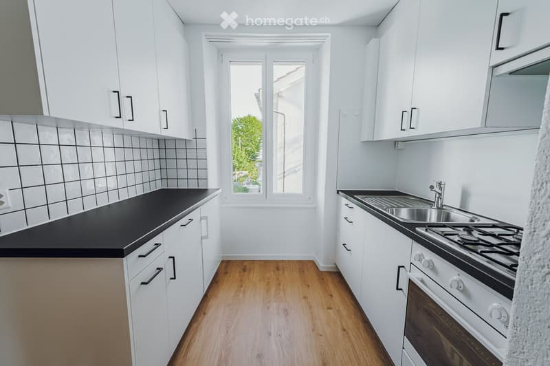 Modern kitchen with white cabinets, black countertops, and wooden flooring. Features a sink, stove, and oven.