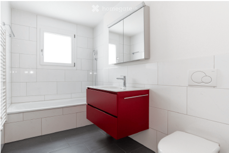 Modern bathroom with white tiles, red cabinet, sink, mirror, and toilet.