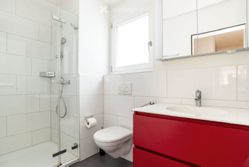 Modern bathroom with white tiles, a red vanity, a toilet, a sink, a mirror, and a glass-enclosed shower.