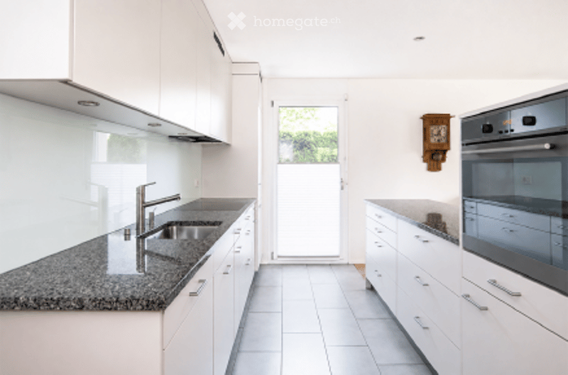 Modern kitchen with white cabinets, granite countertop, stainless steel sink and faucet, built-in oven, and tiled flooring.