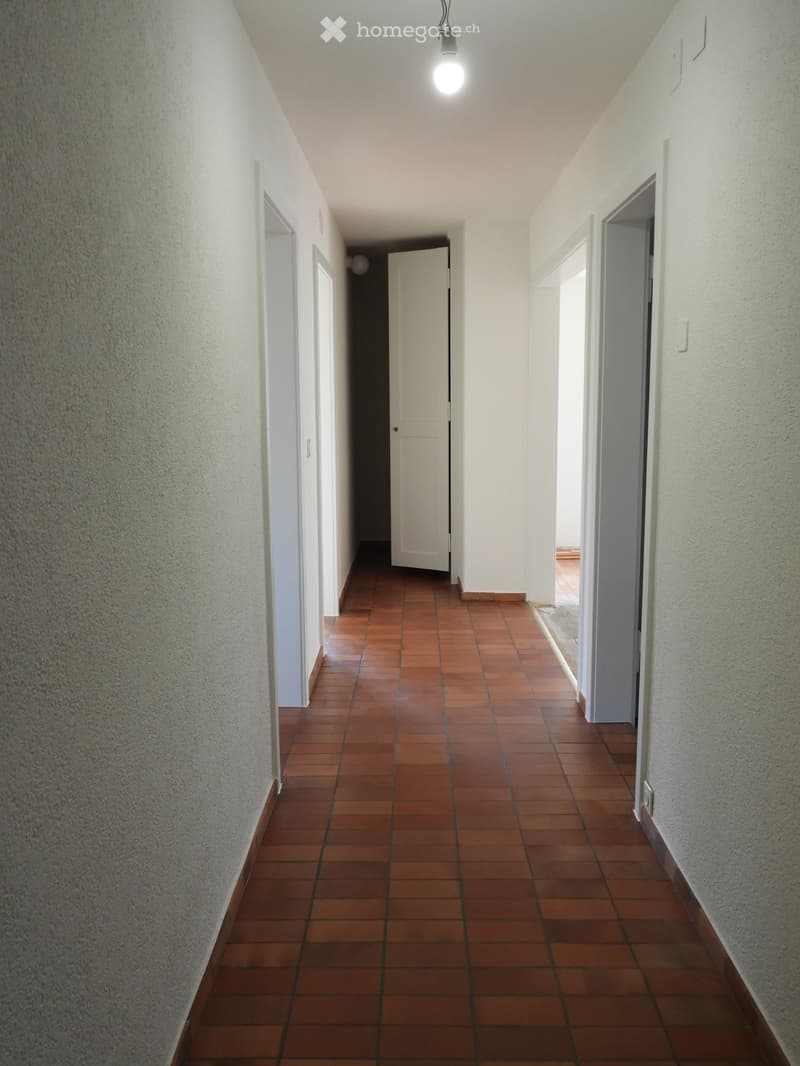 Empty hallway with white walls, brown tiles, and white doors