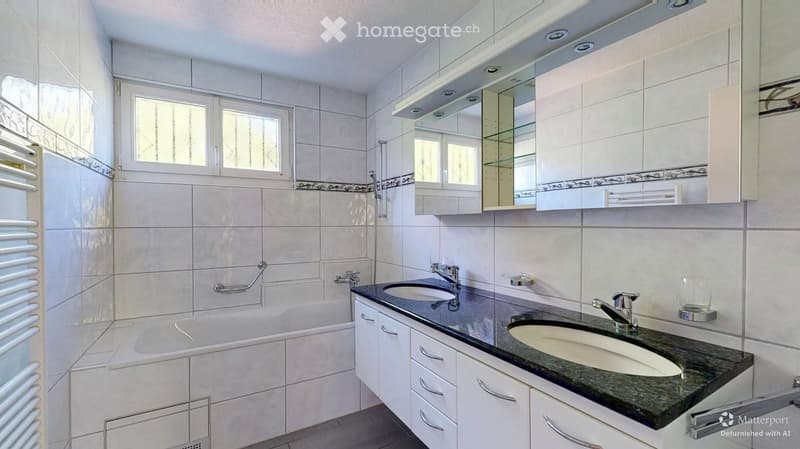 Modern bathroom with white tiles, a bathtub, double sink, mirrored cabinet, and a radiator.