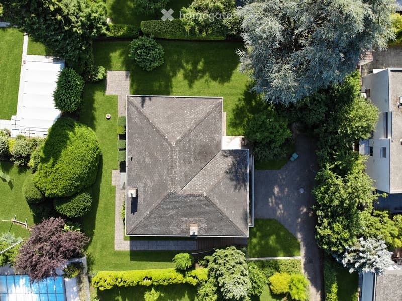 Aerial view of a house with a well-maintained garden, driveway, and swimming pool.