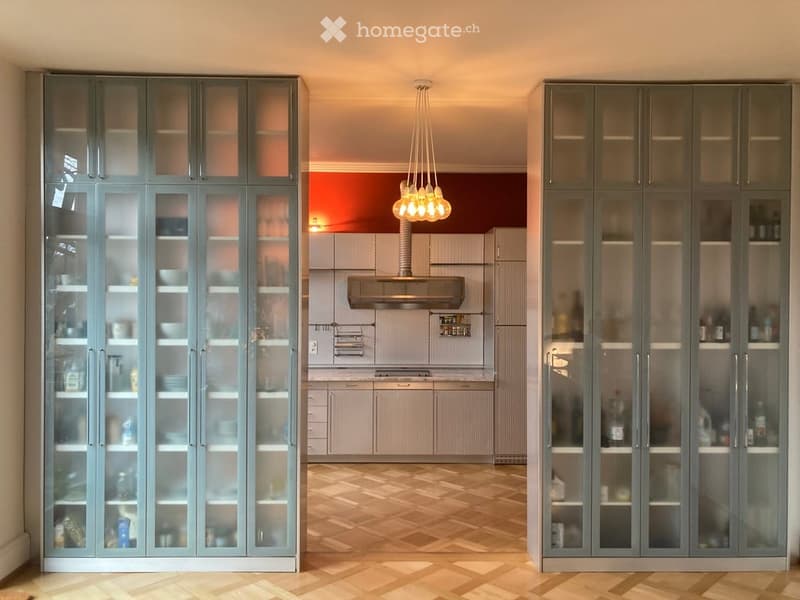 Modern kitchen with grey cabinets, glass-fronted display cabinets, pendant light, and range hood.