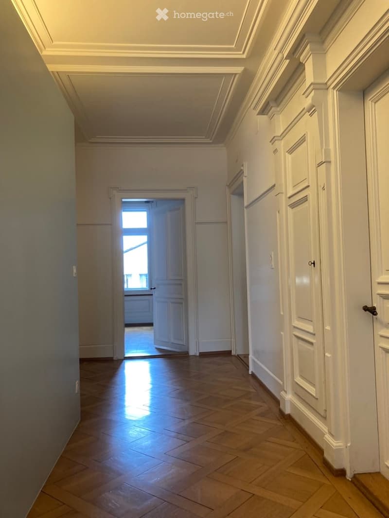 Empty hallway with wooden flooring, white walls, and doors leading to other rooms.