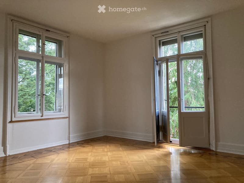 Empty room with wooden flooring, large windows, and an open door leading to a balcony area.