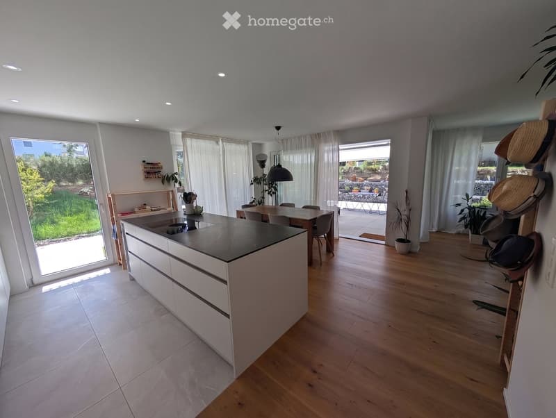 Modern kitchen with white cabinets, island, dining area, large windows, and outdoor access.